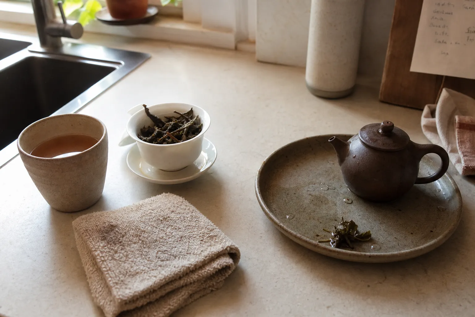 A cup, towel, and tea vessels arranged on a counter for checking serving size, cleaning, and pour comfort